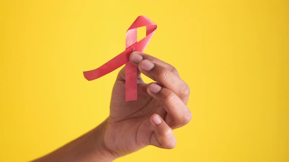 Hand Holding Red HIV Ribbon Against Yellow