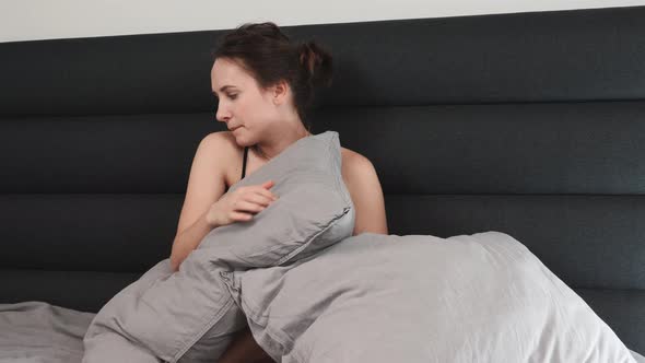 Sad woman sitting on bed hugging pillow