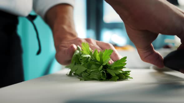 Professional kitchen of the restaurant, close-up: The chef cuts the greens herbs finely with a knife