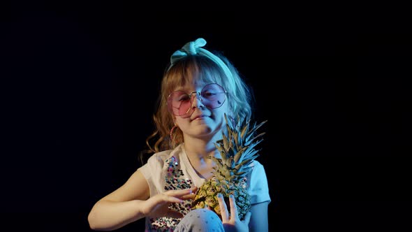 Trendy Girl in Futuristic Glasses Hiding Behind Pineapple on Black Background Smiling Fooling Around