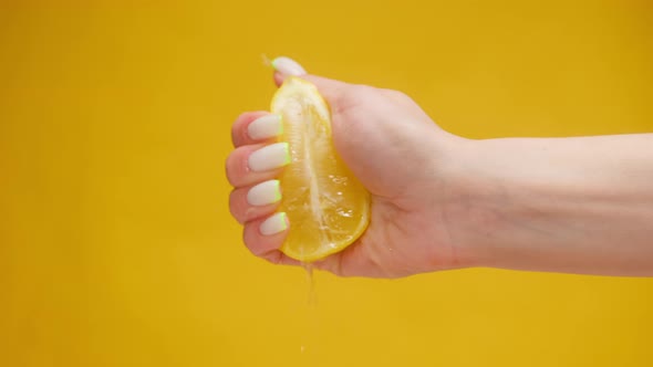 Closeup of Squeezing Orange Juice with Splashes By Female Hand on Orange Background Making Citrus