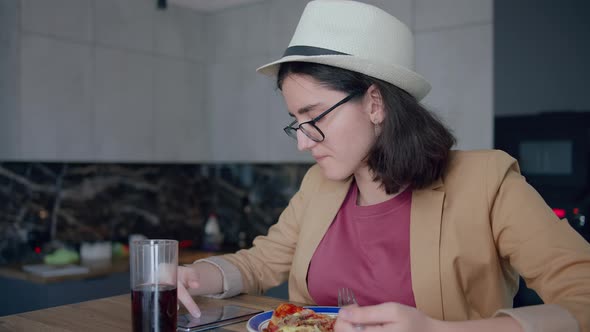 Portrait of a Pretty Girl in a Hat and Glasses Eating and Browsing a Mobile App