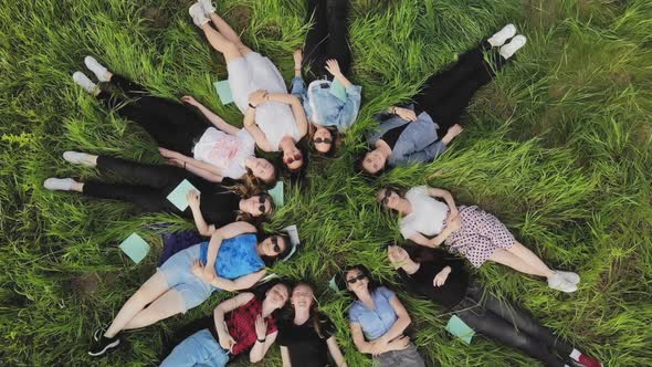 Girls Students Lie on the Grass in a City Park with Notebooks