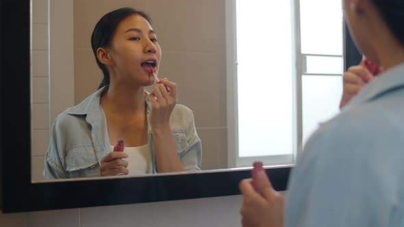 Asian woman using lipstick make up in front mirror ready to working in bathroom at home.