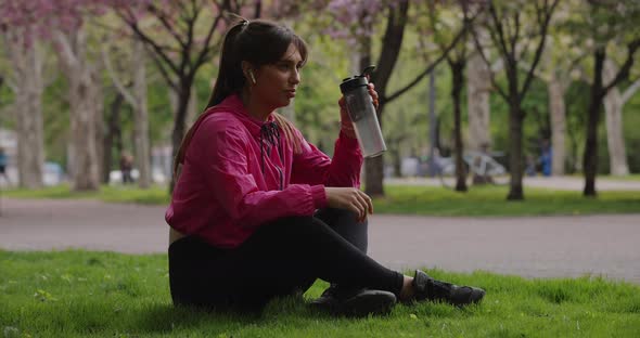 Sporty Woman Drinking Water From Shaker Sitting in the Park