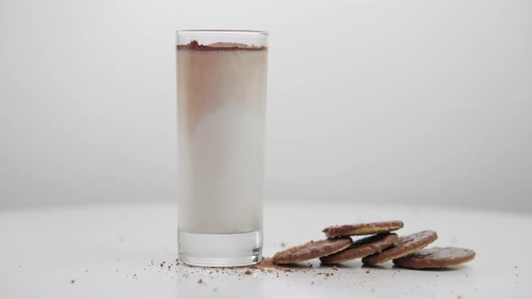 Hand Putting Glass with Milk As Chocolate Powder Falling in Liquid to Cookies on Table