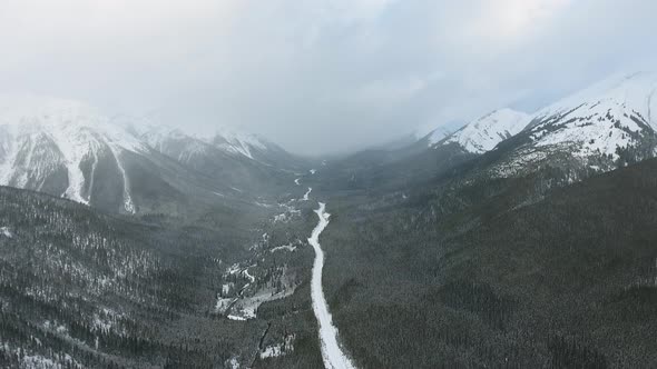 Overhead aerial shot of winter forest in mountains and a long road to the horizon in Alberta, Canada