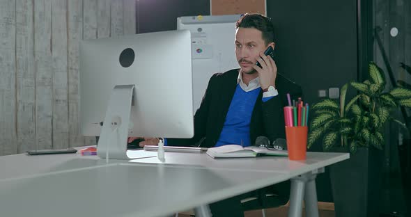 Businessman in the Office in Front of the Computer Talking on the Phone