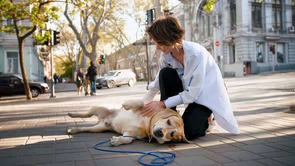 Portrait of Young Stylish Hipster Girl Petting a Retriever Dog Outdoors in City Center During Sunny