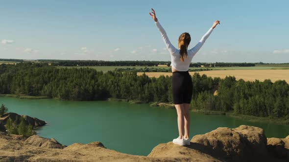 Athletic Slender Woman in Black Bicycles or Leggings and White Turtleneck or Top Stands on the Edge