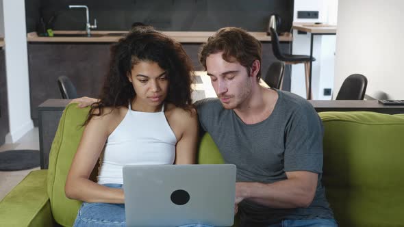 Couple Quarreling While Using Laptop While Sitting on Sofa at Home