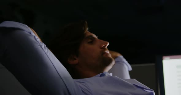 Side view of young Caucasian male executive with hands behind head sitting at desk in modern office