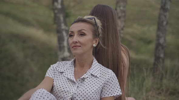 Portrait of Confident Beautiful Caucasian Adult Woman Sitting Back To Back with Adult Daughter