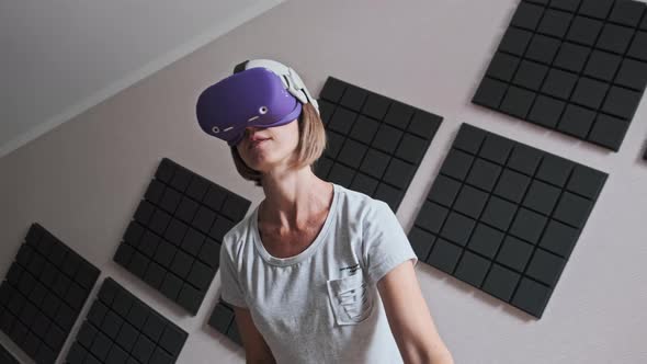 Young Woman in a VR Helmet Plays a Game at Home