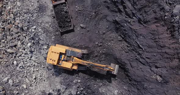 Excavator Loads Coal into Large Dump Truck at Open Pit Coal Mining Area.