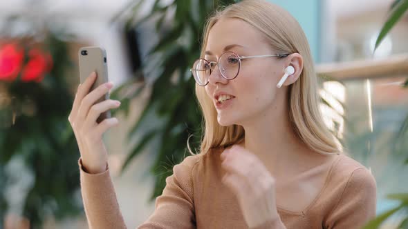 Excited Young Attractive Millennial Girl with Wireless Headset Chat By Video Call Use App on Phone