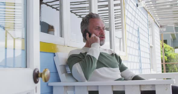 Happy caucasian mature man siting on the terrace and using smartphone