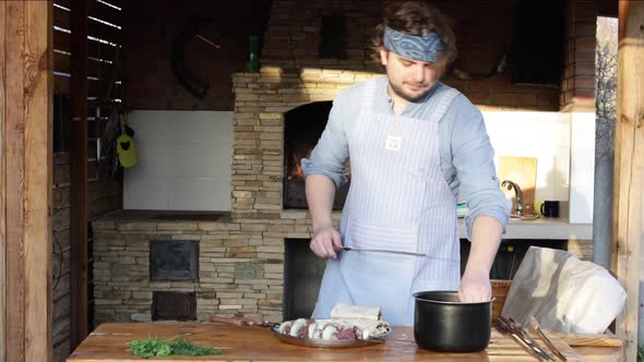 A Man in an Apron Strings Pieces of Meat on a Skewer and Makes a Kebab From It Near the Fireplace