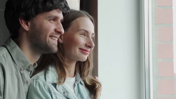 Young and Happy Couple Standing Together Looking Out of a Window