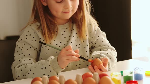 Little child girl with rabbit ears decorates Easter eggs with colored food paint.