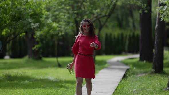 Positive Woman is Walking in Park Alone Wearing Fashion Sunglasses Carrying Bottle with Water