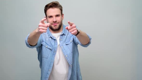 Portrait shot of young caucasian man pointing with his finger to the camera over grey background