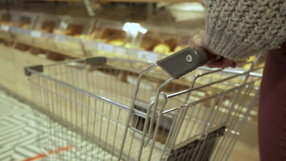 Closeup of a Young Female Shopper's Hands Moving an Empty Cart Through the Aisles of a Supermarket