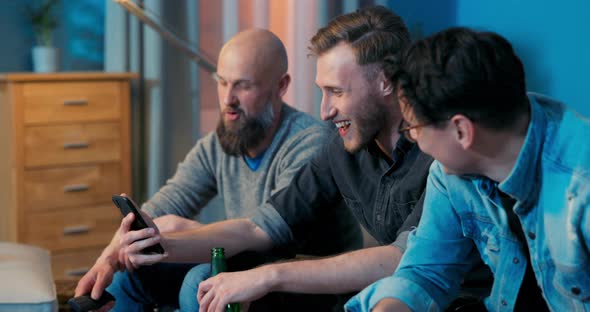 Three Men are Relaxing on the Living Room Couch in the Evening in Front of