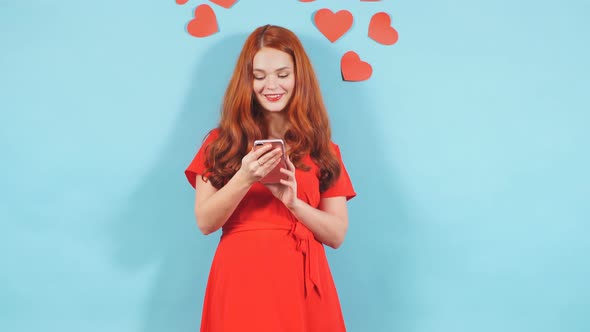 Portrait of Young Surprised Woman with Red Hair Looking at Screen of Mobile Phone in Shock.