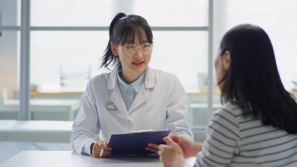 Asian Female Doctor Consulting Woman in Clinic