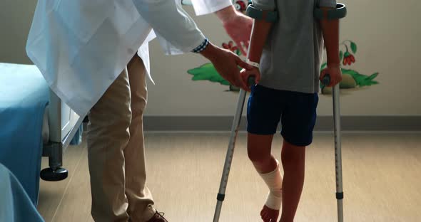 Male doctor assisting injured boy to walk with crutches