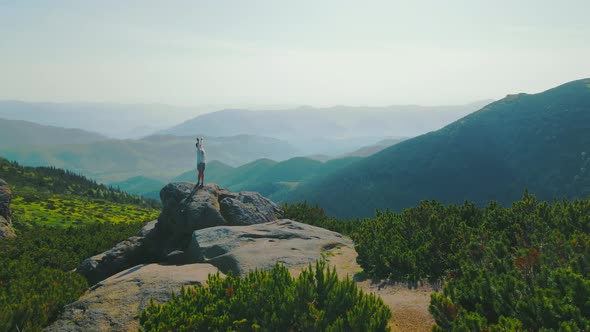 Happy Woman Hiker in the Mountains Rotating Standing on a Rock with Arms Raised