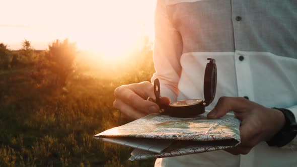 A man with a map and a compass in his hands is looking for a way. Sunset.