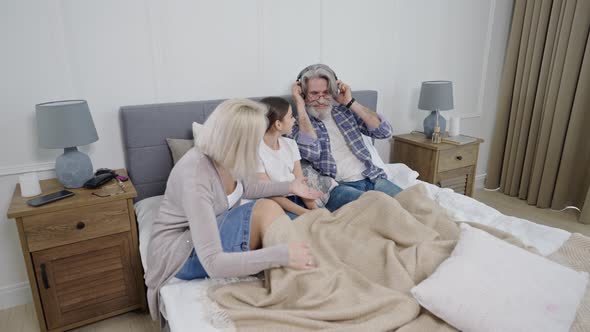 Cute Little Girl Granddaughter Listening Music with Grandparents While Relaxing Together in Bed