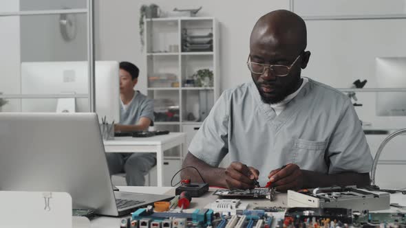 African American Engineer Testing Electronics with Multimeter and Laptop