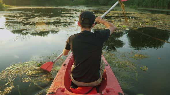 Fitness male tourist is kayaking in red canoe along calm river at sunset.