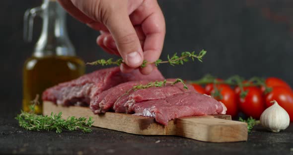 The Man's Hand Puts Thyme on Pieces of Raw Beef. 