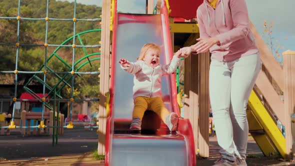 A cute little baby is rolling down a children's slide.