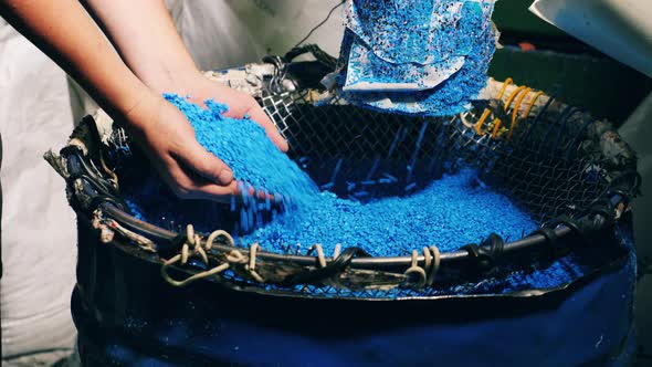 Blue Plastic Particles Sifting Between Someone's Fingertips