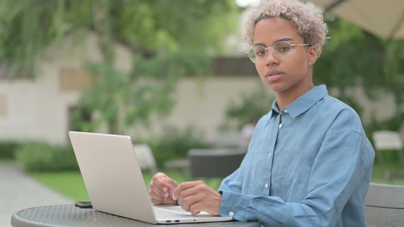 Young African Woman with Laptop Looking at Camera in Outdoor Cafe