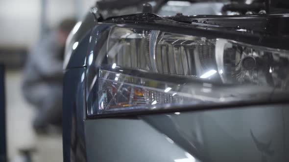 Close-up of Car Headlight with Blurred Auto Mechanic Tightening Screws on Wheel. Repair or Tuning of