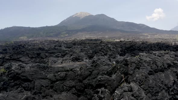 Flying low level over solid, black lava towards a volcano