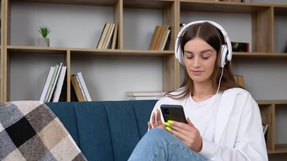 Woman Listening Music in Headphones While Sitting on Sofa in Room