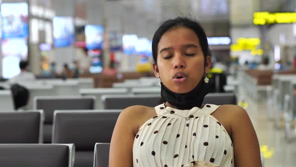 Asian Woman Sitting in the Waiting Area of Airport Taking Off Mask and Breathing