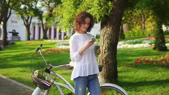 Portrait of a Young Woman Typing a Message Using Her Smartphone Standing in the City Park Near Her