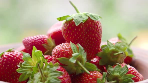 Strawberry on a Clay Plate Covered with Water Droplets are Spinning Over Blurred Natural Background