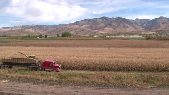 Aerial view flying over combine loading truck towards the mountains