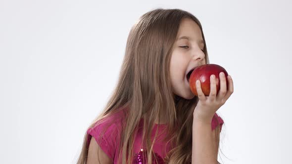 Little Girl on White Eats a Big Red Apple. A Girl Bites a Piece of Red Ash and Tastes It