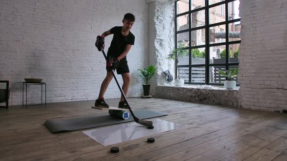 A Cute Boy Hockey Player Stands on a Balance Board and Trains with a Stick and Puck on a Slippery