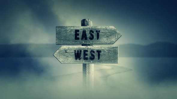 Old Wooden Sign On A Middle Of A Cross Road With The Words East Or West